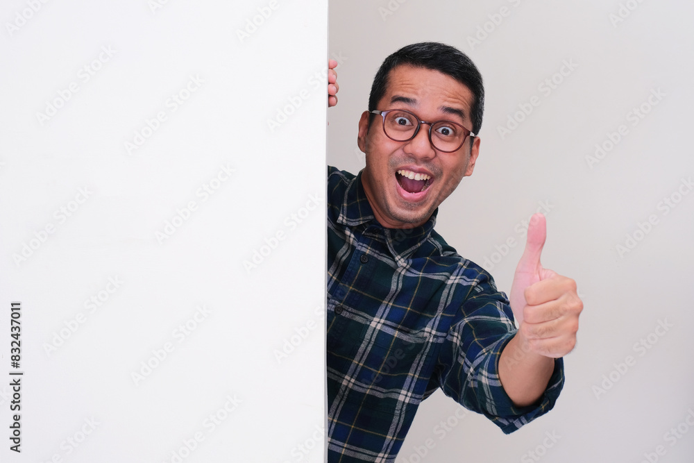 A man peeking behind white billboard with excited expression and give thumbs up A man peeking behind white billboard with excited expression and give thumbs up