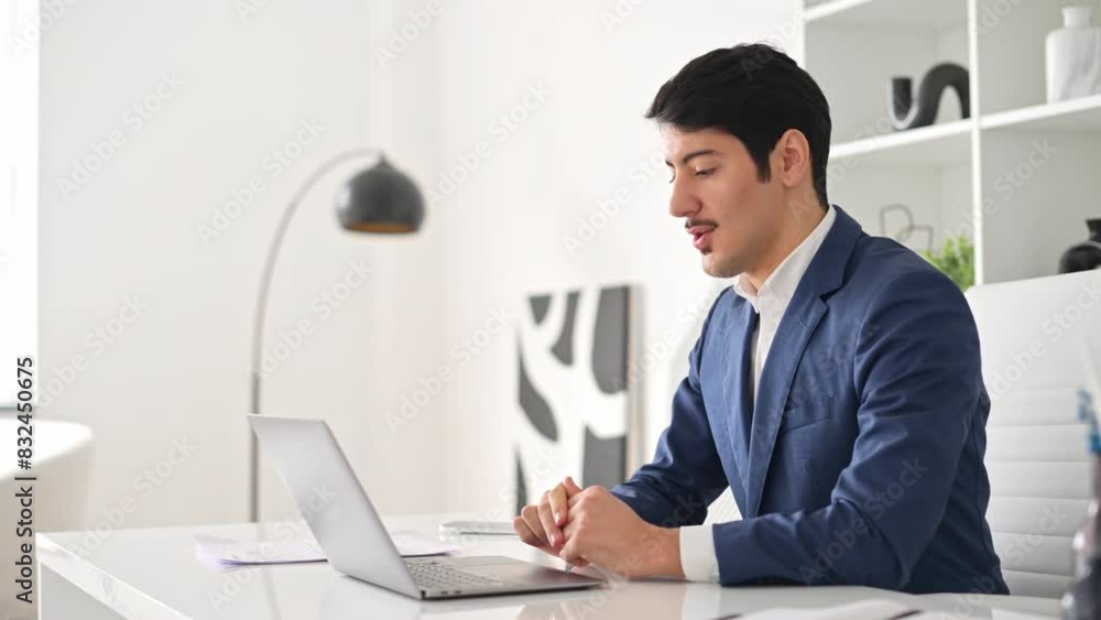 A jovial Hispanic businessman waves at his laptop screen during a video call, a representation of friendly remote communication and modern work practices. Virtual meeting concept A jovial Hispanic businessman waves at his laptop screen during a video call, a representation of friendly remote communication and modern work practices. Virtual meeting concept