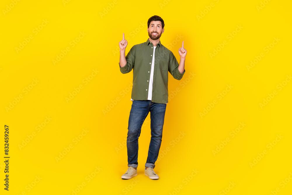 Full size photo of nice young man direct fingers up empty space wear shirt isolated on yellow color background
