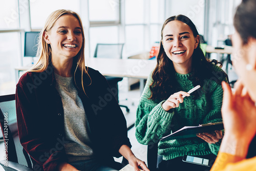 Cheerful female designers laughing during morning briefing in office interior.Positive colleagues discussing productive strategy for developing own businee startup project during friendly meeting photo