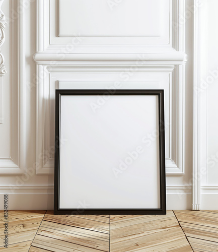 Blank Picture Frame on Elegant White Wall. A blank black picture frame leaning against an ornate white wall with wooden herringbone flooring, ready for artwork.