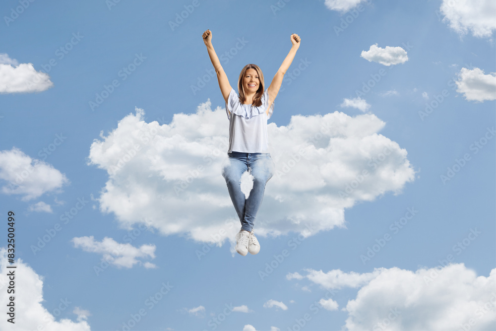 Fototapeta premium Happy young woman sitting on a cloud and raising arms