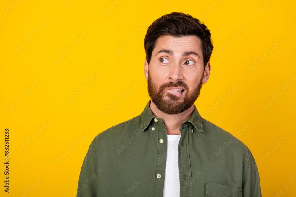 Obraz premium Photo of nice young man bite lips look empty space wear khaki shirt isolated on yellow color background