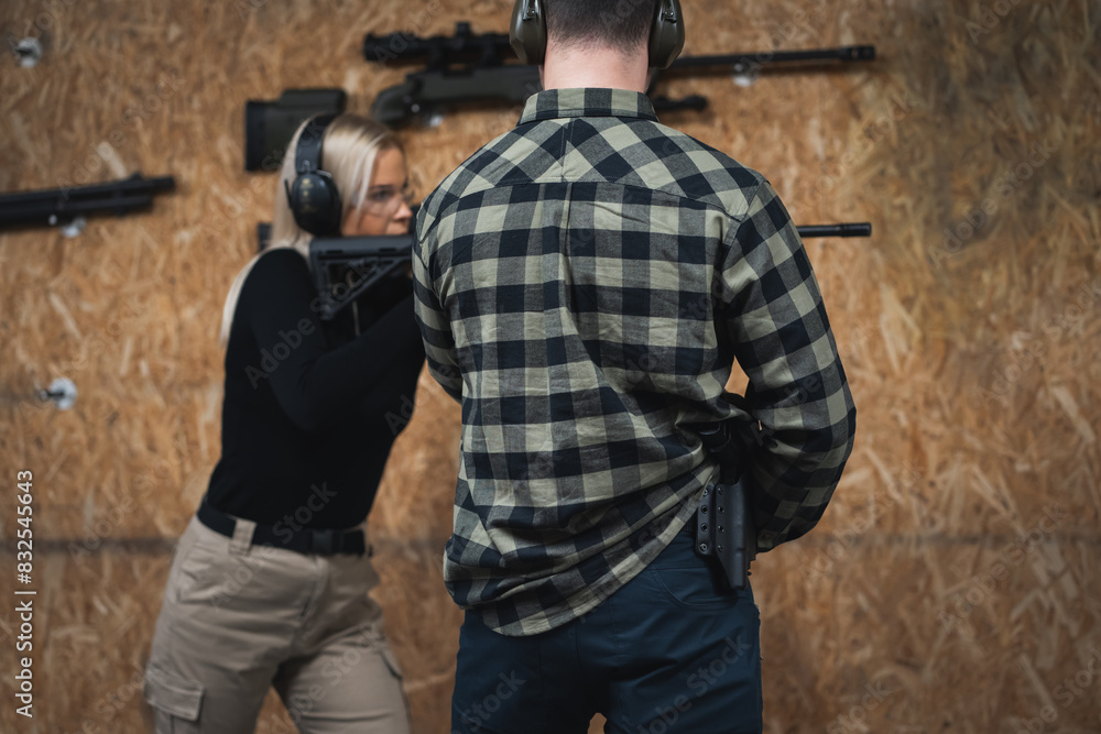 Fototapeta premium A young girl learns to shoot a tactical rifle at a shooting range with an instructor.