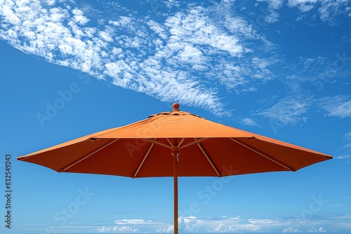 A striking orange beach umbrella stands out under a clear blue sky with scattered clouds