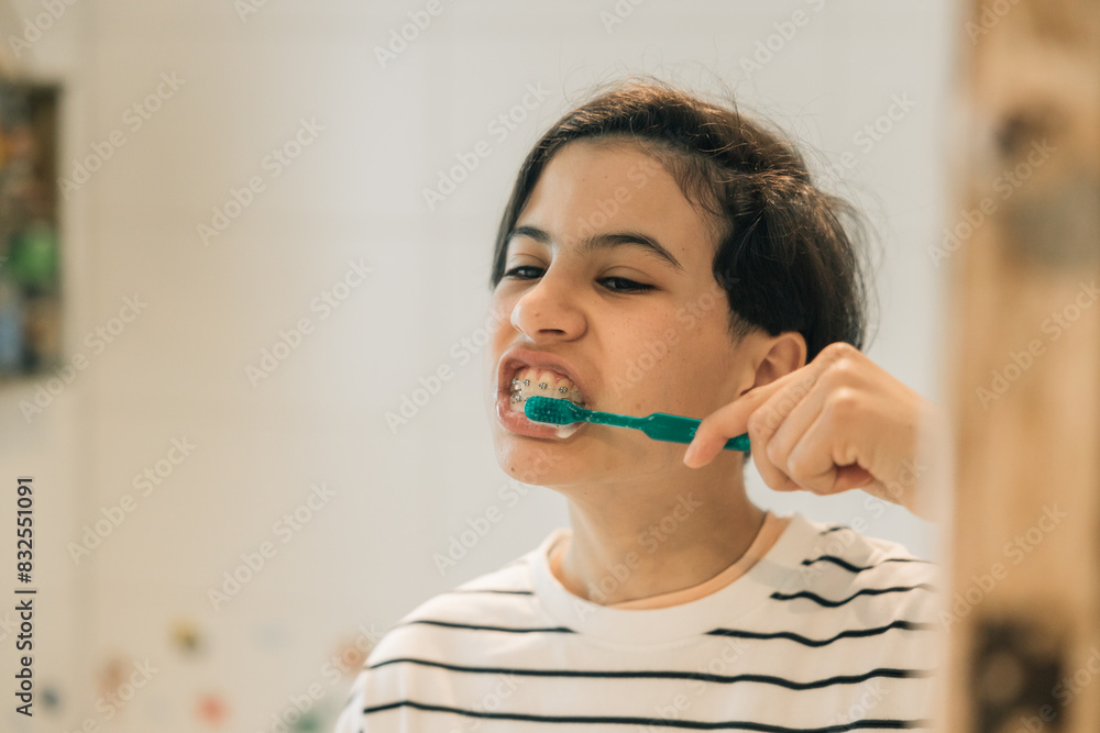 Teenage girl brushing her teeth with a green toothbrush looking at herself in the bathroom mirror at home Teenage girl brushing her teeth with a green toothbrush looking at herself in the bathroom mirror at home