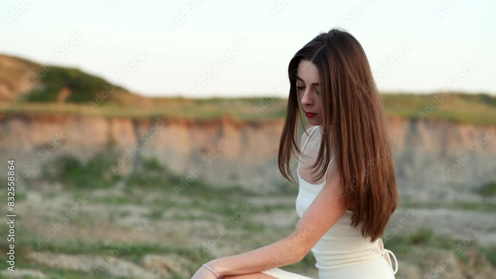 The brunette girl in a white fitted dress touches the palm of her hand to the ground and rises smoothly. The girl merges with nature. The brunette girl in a white fitted dress touches the palm of her hand to the ground and rises smoothly. The girl merges with nature.