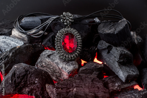 red stone pendant with diamonds around it lies on burning coals photo