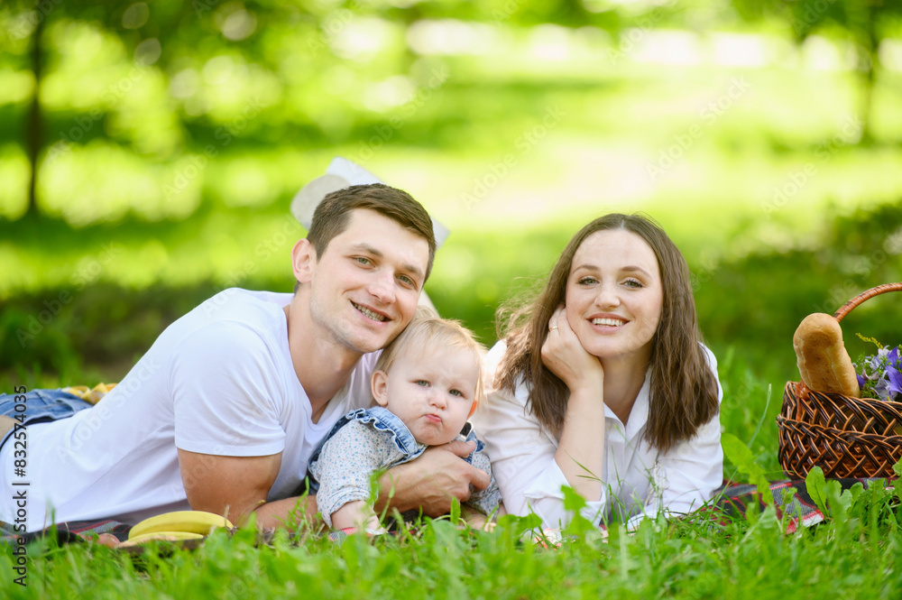 Mom and dad lie next to child on grass, smiling joyfully, enjoying sunny day together. Family love and spending time, enjoying nature. Concept for outdoor fun, family picnic