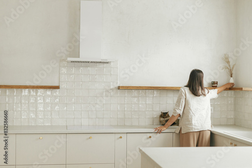 Φωτογραφία Stylish woman with her cat unpacking and decorating shelves with utensils in new minimal white kitchen