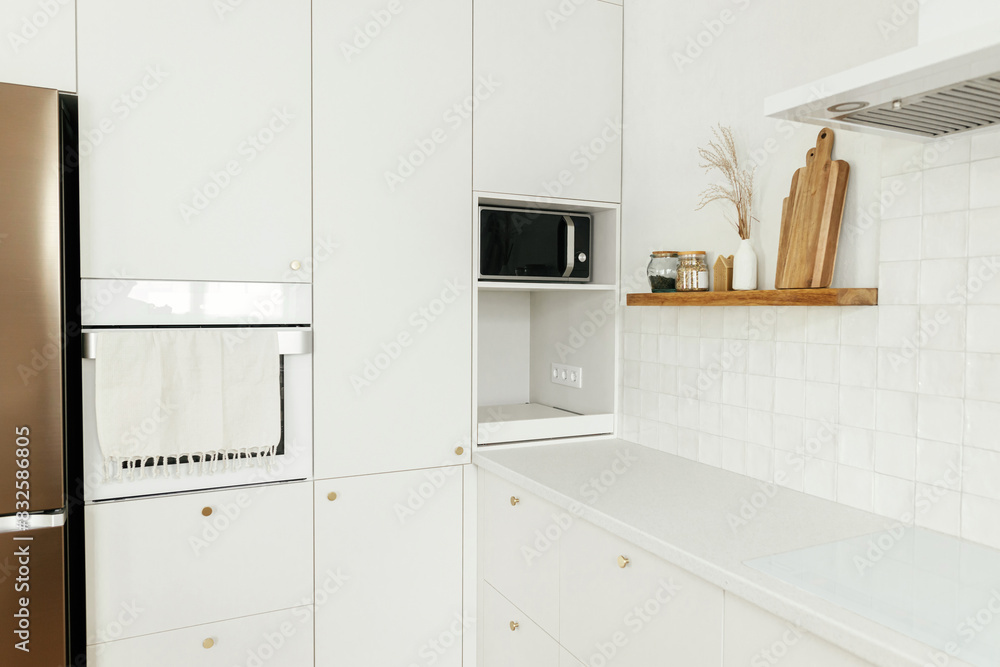 Modern kitchen interior. Stylish white kitchen cabinets with brass knobs, wooden shelves with utensils and appliances in new scandinavian house. Modern minimal kitchen design Modern kitchen interior. Stylish white kitchen cabinets with brass knobs, wooden shelves with utensils and appliances in new scandinavian house. Modern minimal kitchen design
