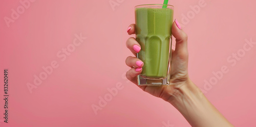 Woman hand with pink nails holding green smoothie glass isolated on pastel background photo