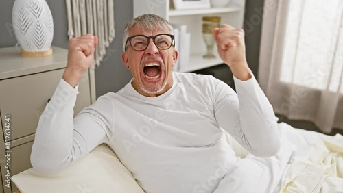 Angry middle age grey-haired man, fists raised in fury, mad and frustrated in his bedroom. rage and aggression frame his expression, painting a picture of intense emotion. photo