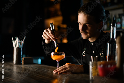 Bartender adds a piece of zest to a cocktail glass, holding it with bar tweezers