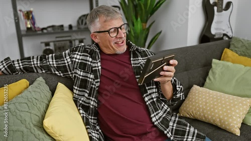 Grey-haired man reading tablet on sofa in cozy living room photo