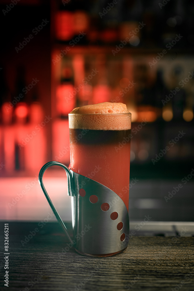 Glass tumbler with a metal stand filled with a brown foamy drink Glass tumbler with a metal stand filled with a brown foamy drink