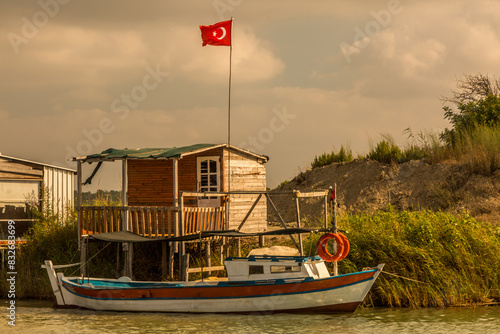 Foto A single wooden boat, moored on a riverbank next to an old wooden hut in Antalya