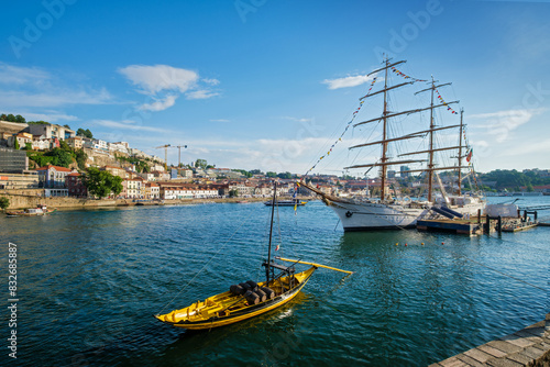 View of Vila Nova de Gaia city with sailing ship and traditional boat with port wine barrels and Douro river with tourist boats on sunset. Porto, , Portugal