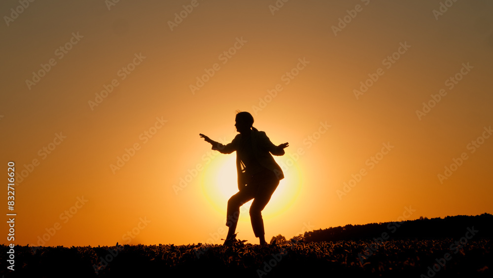 At sunset, an energetic young woman is silhouetted as she dances the twist.
