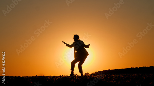 At sunset, an energetic young woman is silhouetted as she dances the twist.