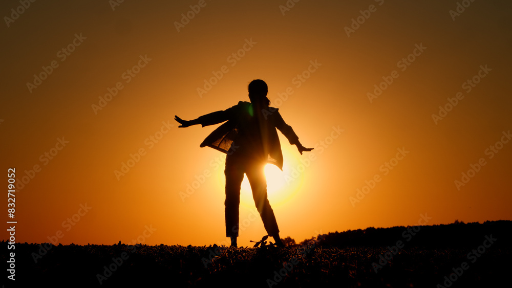 Against an orange sky, a young fiery woman is seen dancing in a field at sunset.