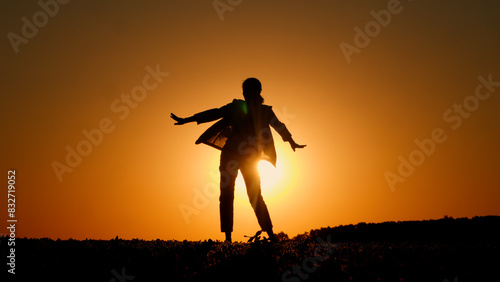 Against an orange sky, a young fiery woman is seen dancing in a field at sunset.