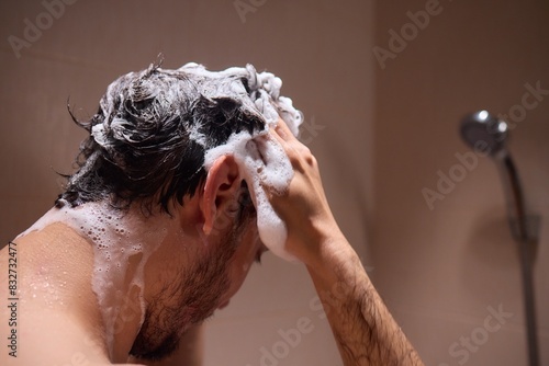 Man washing hair with shampoo in shower, creating foamy lather - personal hygiene care.