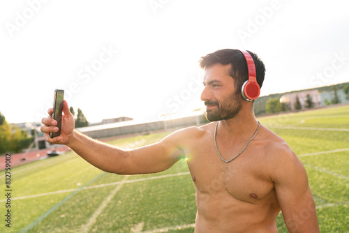 An athlete man takes a selfie with his mobile phone. A man takes a selfie after training in the stadium