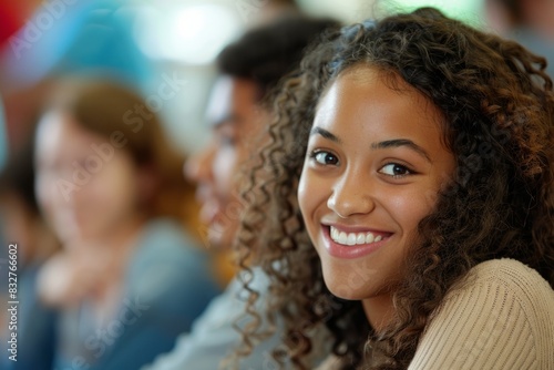 A joyful young woman with curly hair sitting in front of a group of people, engaging enthusiastically during a study session in a classroom