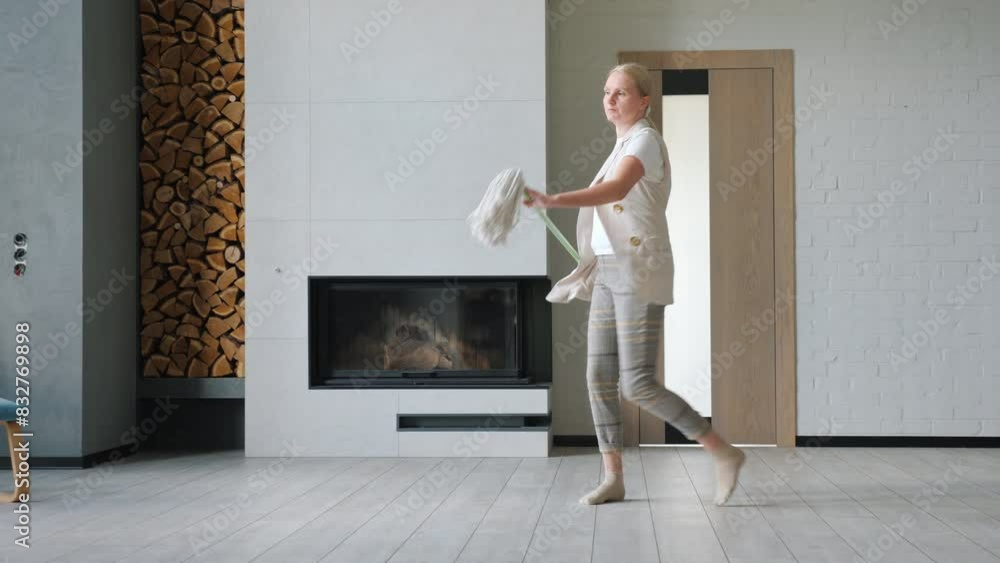 While cleaning her house, a cheerful woman dances with a mop, turning chores into fun. While cleaning her house, a cheerful woman dances with a mop, turning chores into fun.