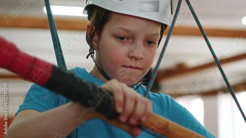 Portrait of a little boy in protective gear, who is concentrating on walking along a thin rope holding onto the crossbar in front of him. High quality 4k footage photo