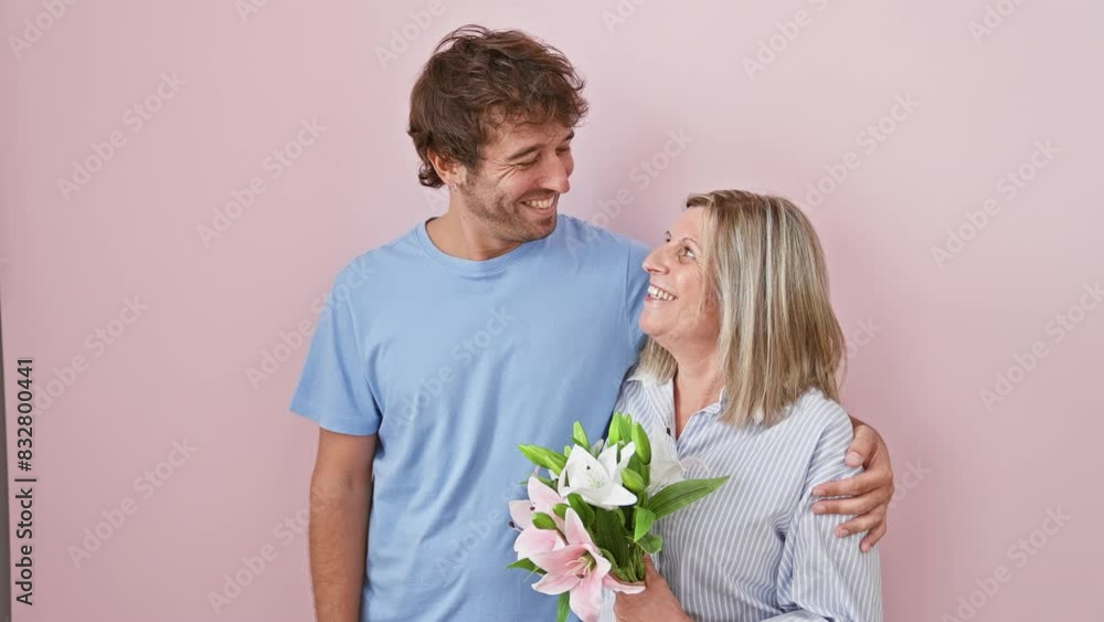 Cheery mother and son sharing a joyful moment over a bouquet of flowers, standing confidently smiling with positive radiance against an isolated pink background Cheery mother and son sharing a joyful moment over a bouquet of flowers, standing confidently smiling with positive radiance against an isolated pink background