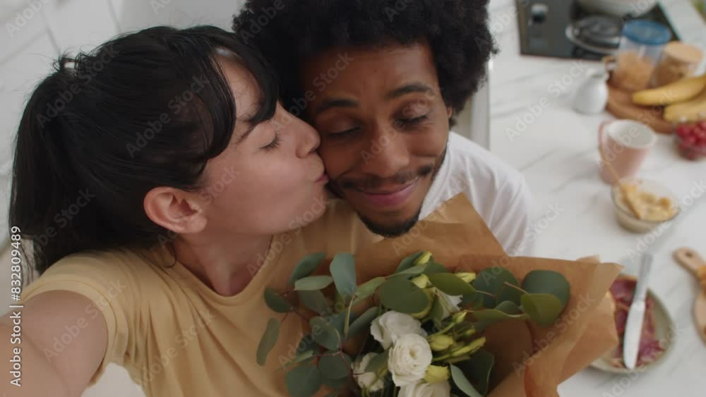 POV of young diverse cheerful couple holding bouquet of white roses and kissing when filming video at home, looking at camera POV of young diverse cheerful couple holding bouquet of white roses and kissing when filming video at home, looking at camera