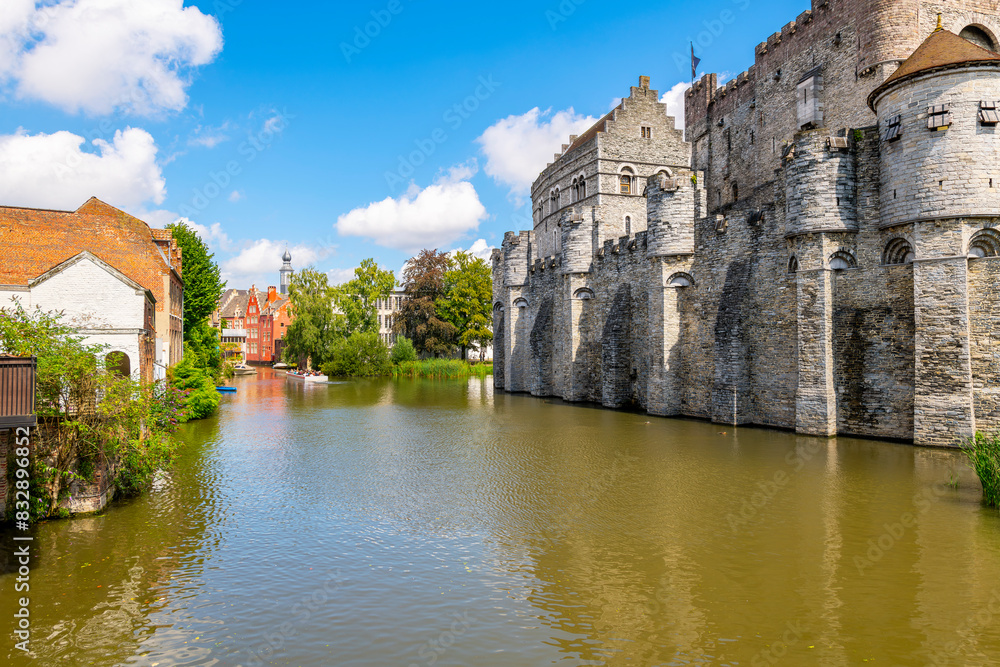 Fototapeta premium A wide section of the Leie River canal alongside the medieval Gravensteen castle on a sunny summer day in the East Flanders city of Ghent, Belgium.