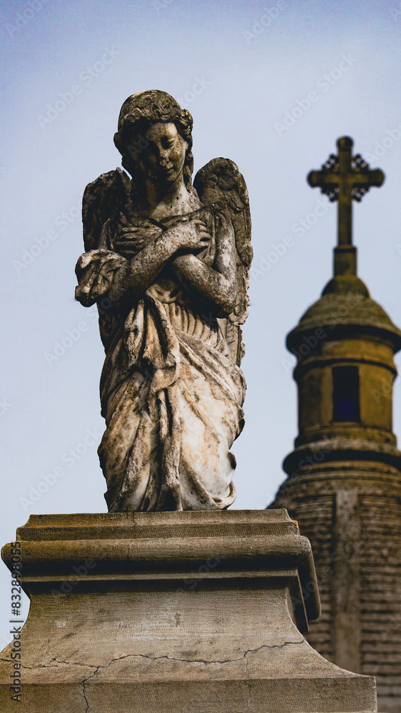 Fototapeta premium Escultura antigua de un angel arrodillado con una capilla detrás 