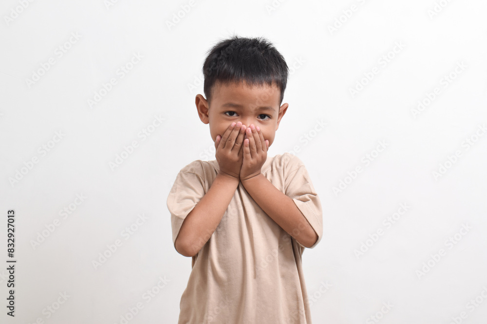 Image of Asian child posing covering his mouth with both hands on a white background. portrait of an Asian boy Image of Asian child posing covering his mouth with both hands on a white background. portrait of an Asian boy