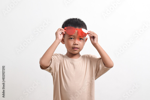 Image of Asian child posing cutely wearing red glasses on white background. portrait of an Asian boy