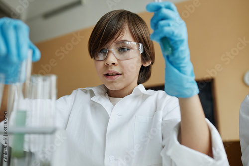Medium closeup of Caucasian boy wearing lab coat and goggles working on experiment during Chemistry lesson at school