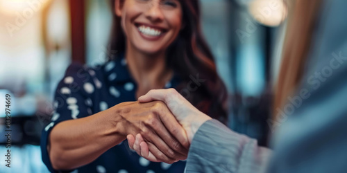 A businesswoman shaking hands with another woman during an office interview, both of them smiling, in a close-up shot. © Duka Mer