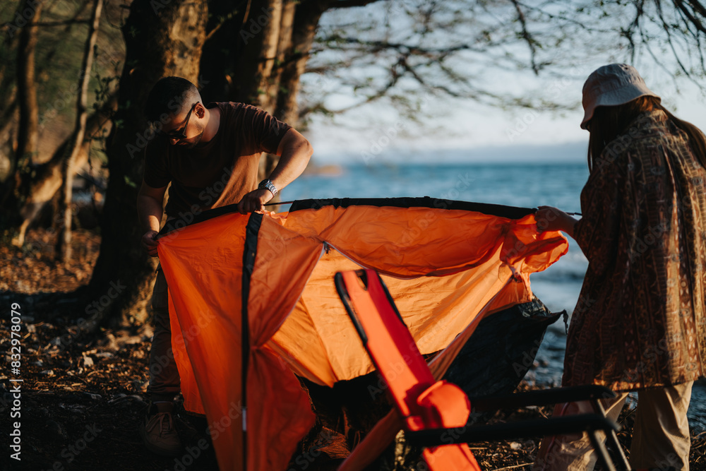 A man and woman pitch a tent near a serene lake, enjoying outdoor activities and relaxation with friends on a beautiful weekend. A man and woman pitch a tent near a serene lake, enjoying outdoor activities and relaxation with friends on a beautiful weekend.