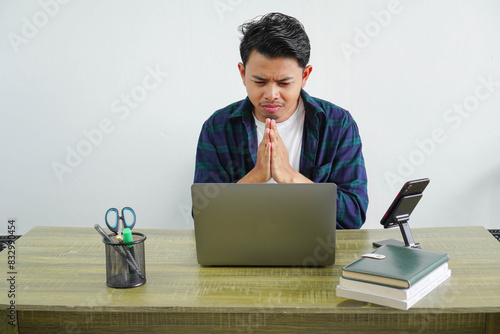 Photos young Asian businessman sitting at workplace apologizes for the mistake