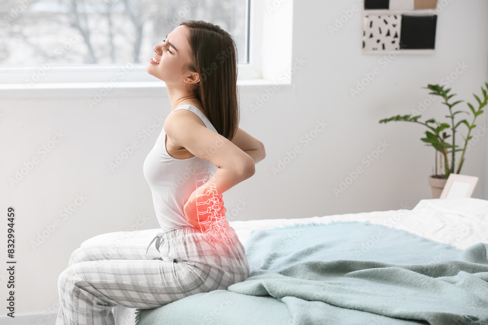 Young woman suffering from back pain in bedroom Young woman suffering from back pain in bedroom