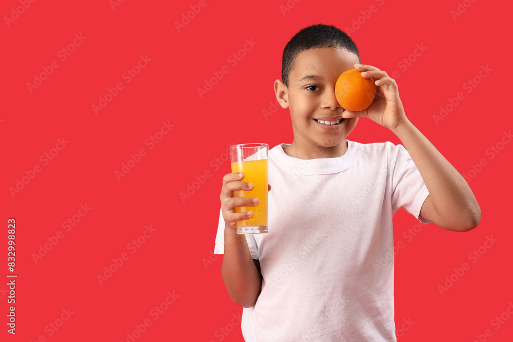 Little African-American boy with glass of juice and orange on red background Little African-American boy with glass of juice and orange on red background