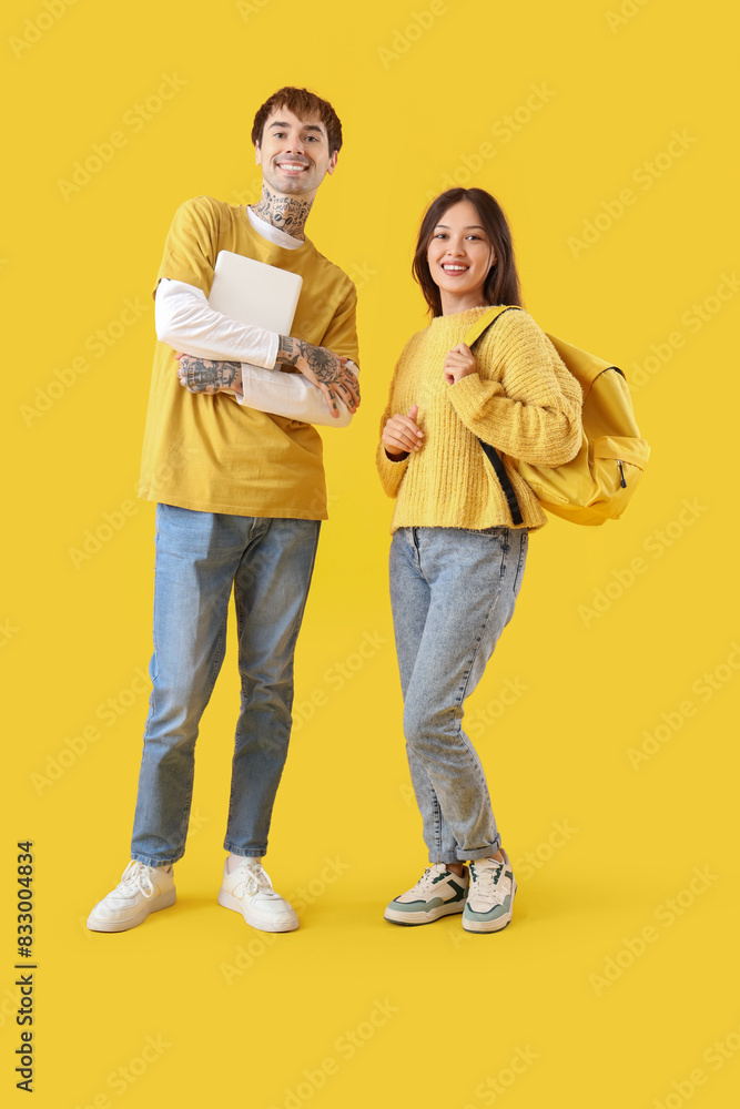 Young students with laptop on yellow background Young students with laptop on yellow background