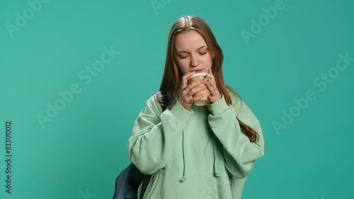 Young girl with backpack yawning, feeling tired, drinking coffee to wake up. Sleepy woman using caffeinated beverage to gain energy, lacking sleep, studio background, camera A