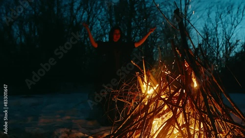 Witch performing witchcraft at bonfire. Mysterious female conjuring in forest during wintery night. She is doing rituals on snow covered landscape on halloween.