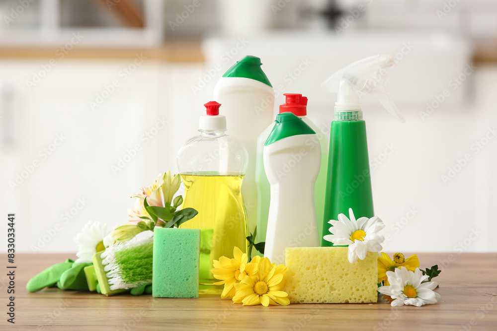 Set of cleaning supplies and spring flowers on wooden table in kitchen Set of cleaning supplies and spring flowers on wooden table in kitchen