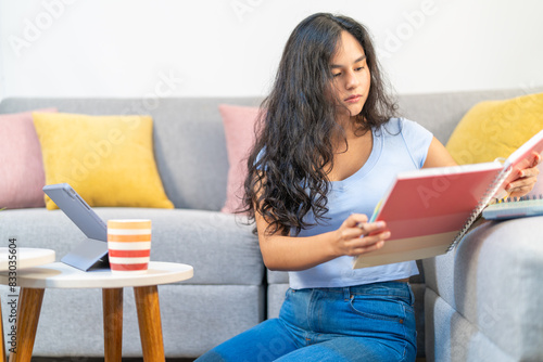 Young student reading a notebook while using tablet at home