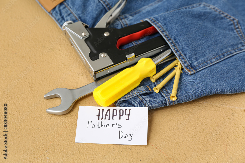 Jeans with tools and greeting card with text HAPPY FATHER'S DAY on beige grunge background Jeans with tools and greeting card with text HAPPY FATHER'S DAY on beige grunge background