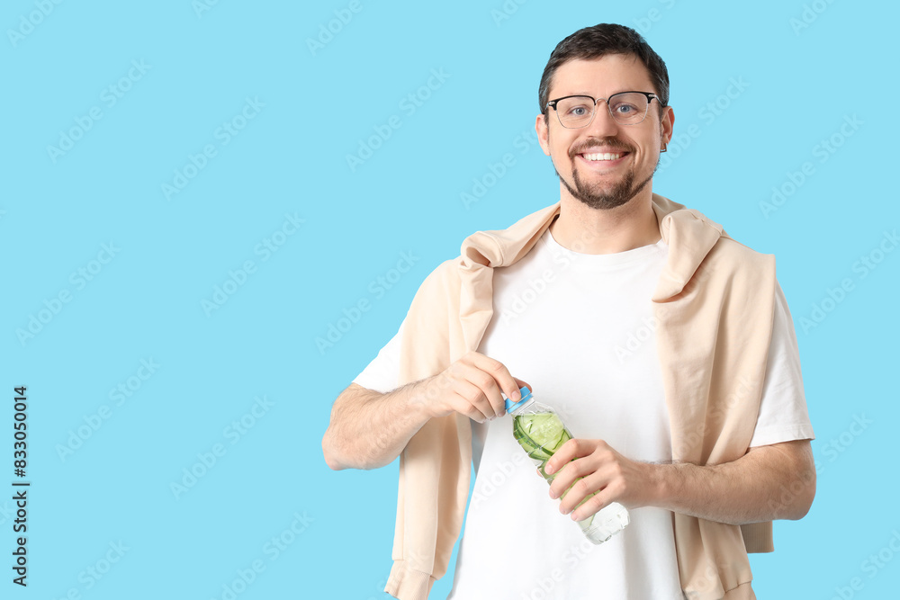 Young man opening bottle of cucumber water on blue background Young man opening bottle of cucumber water on blue background
